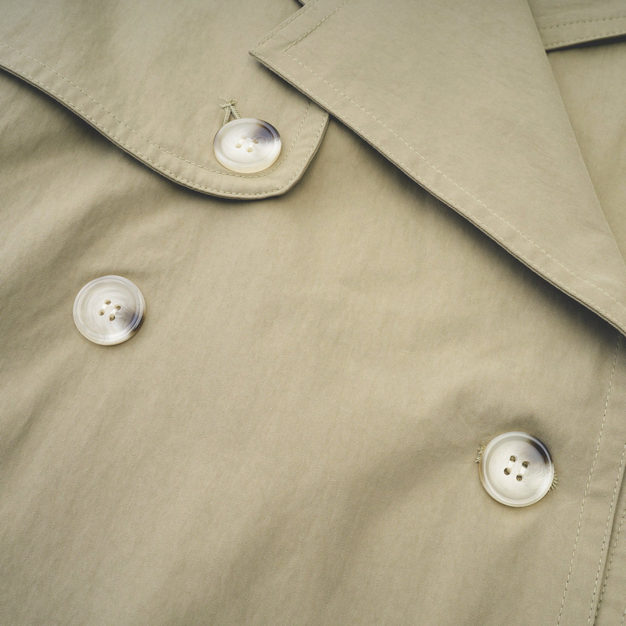Abrigo trench con cinturón de la marca MRNewyork, de corte clásico y color neutro, con detalles de botones y bolsillos visibles.