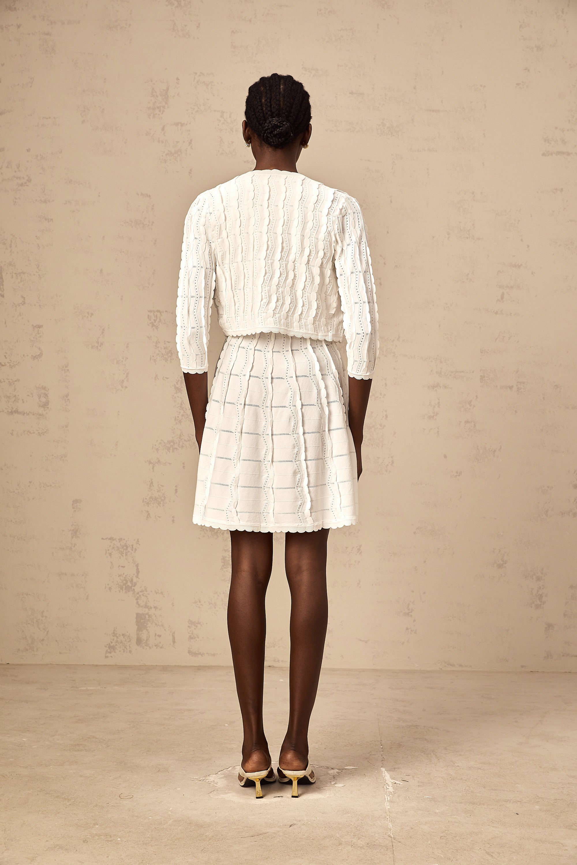 Cardigan de punto blanco Esmée con volantes, estilo abrigado y elegante, para mujer, en un fondo neutro.