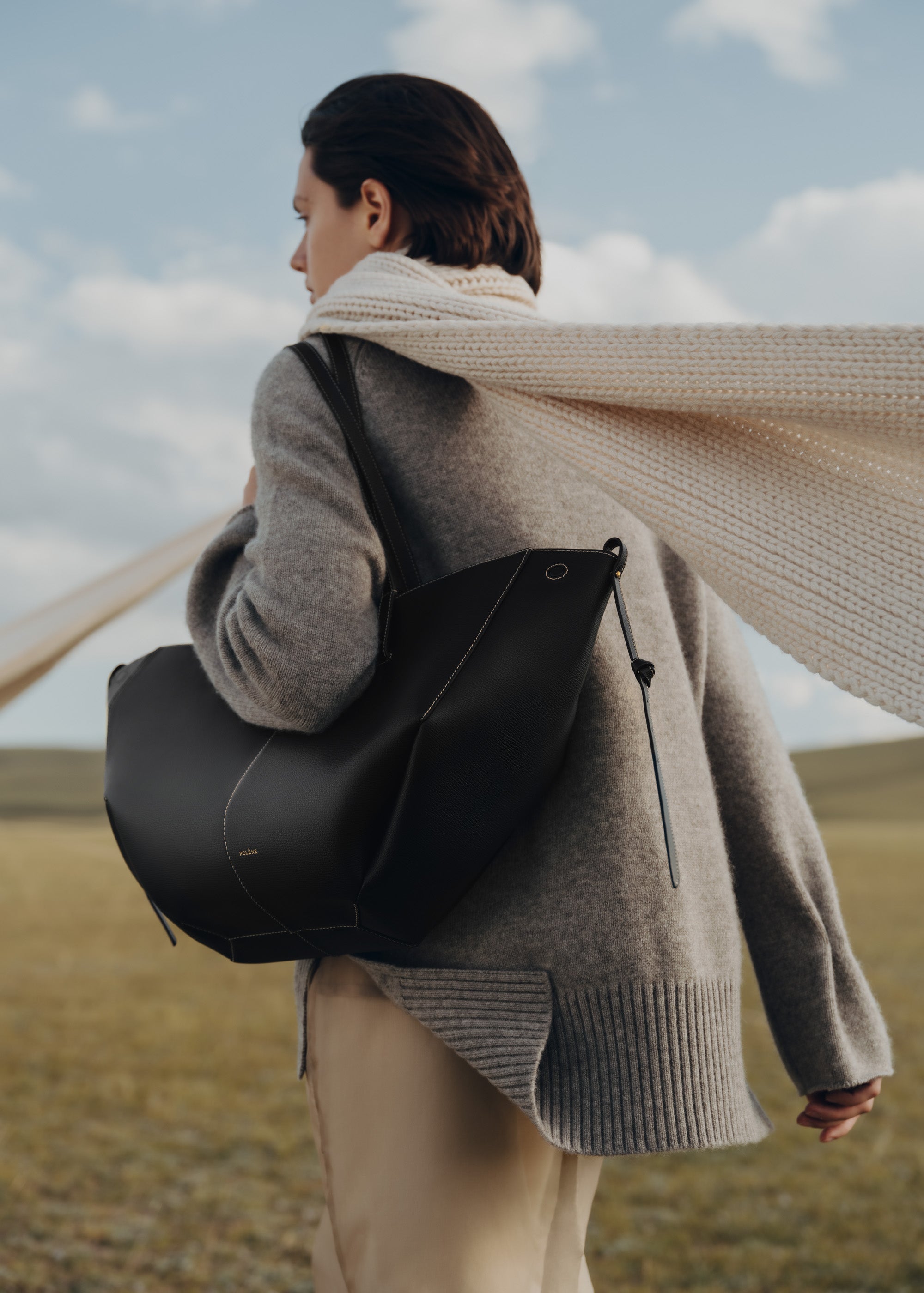 Bolso de mano Polène Cyme en piel negra granulada con costuras contrastadas, diseño elegante y moderno.