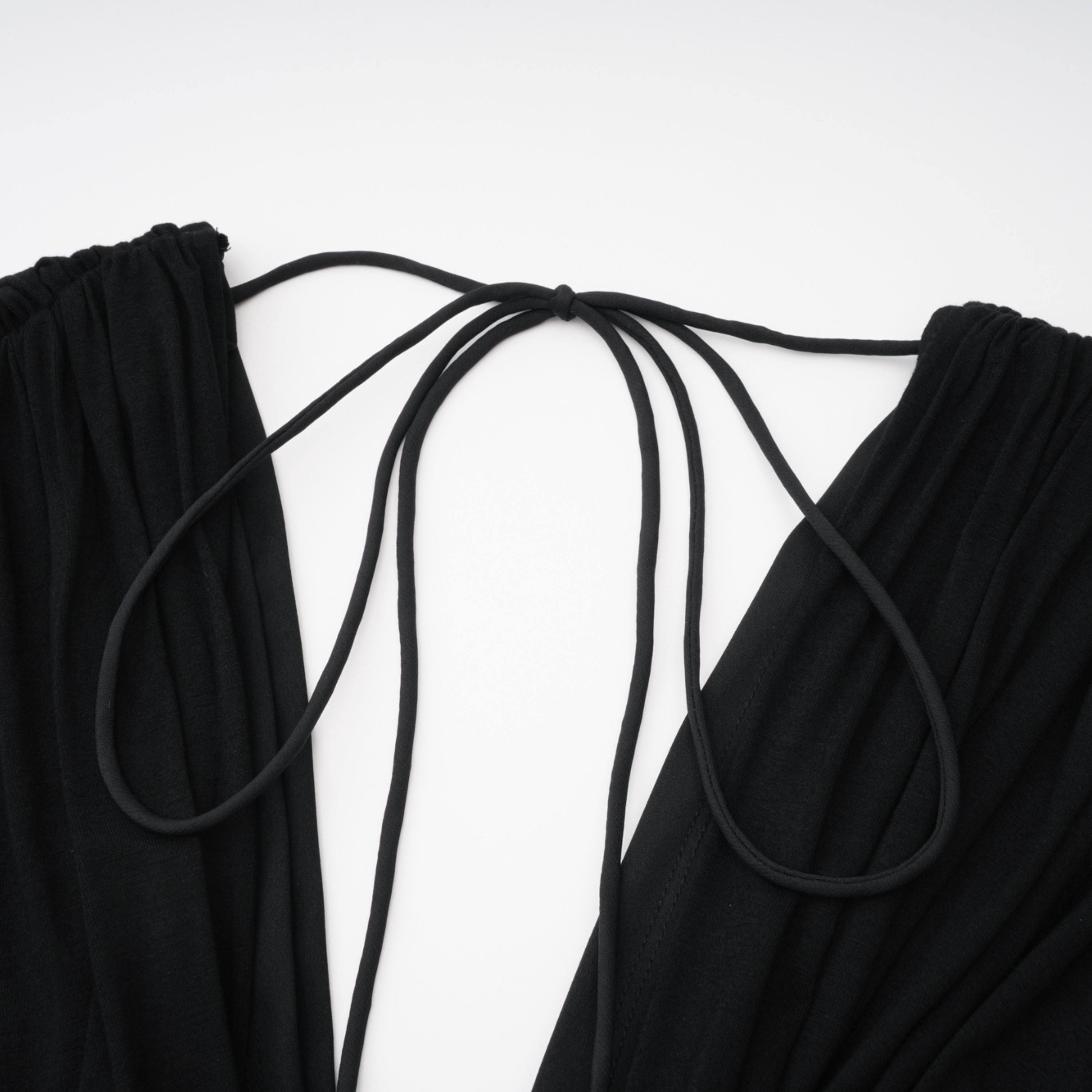 Mono negro Gianina de Bridal con escote en V profundo y diseño drapeado, manga larga y estilo elegante en la imagen.